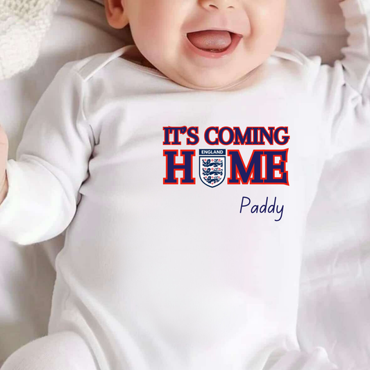 Baby wearing a white onesie with 'It's Coming Home' text and England flag design.