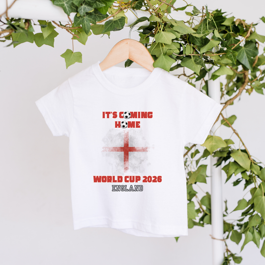 White t-shirt with red text and England flag on a hanger with green leaves in the background