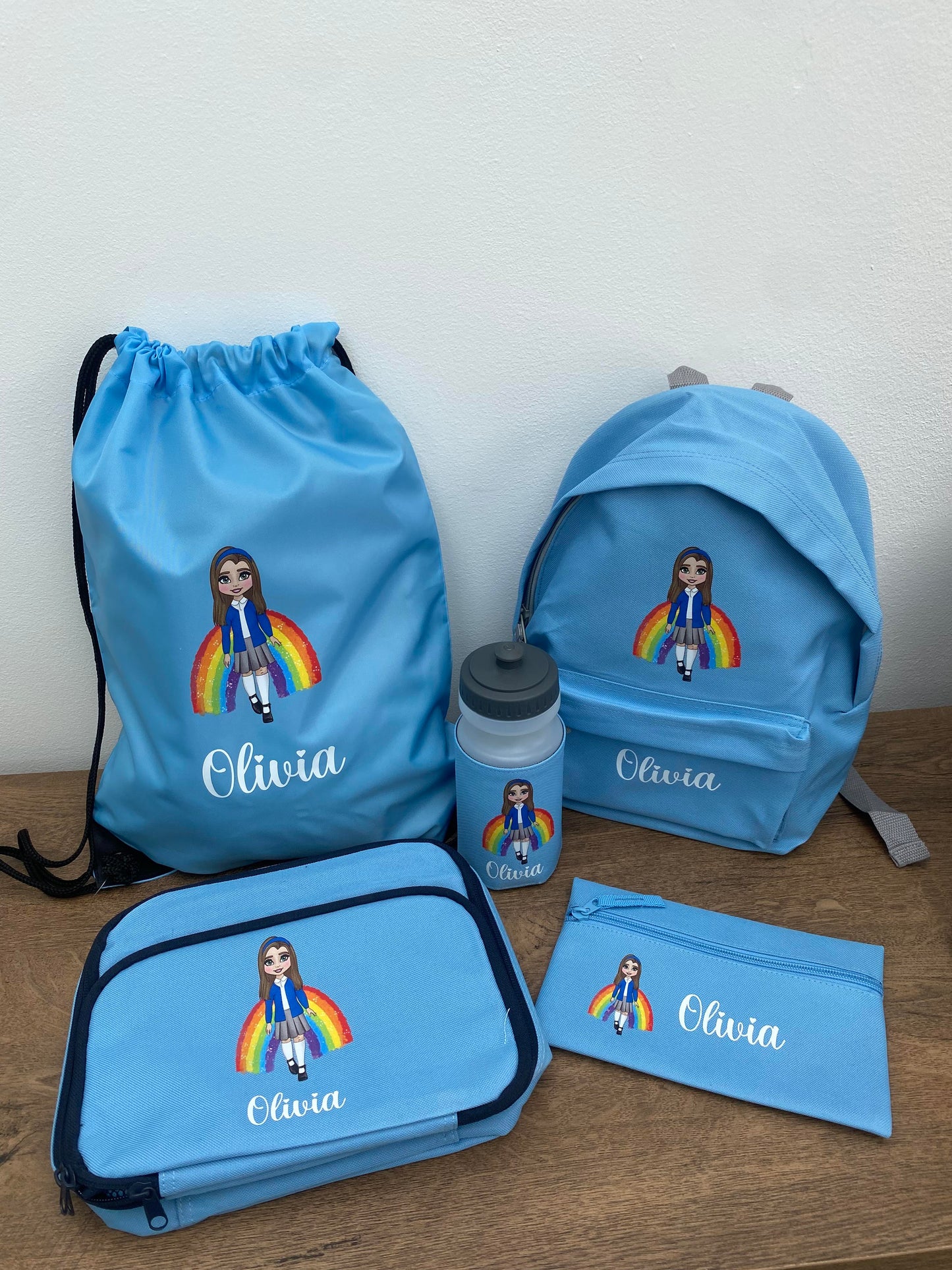Customized school bundle set including a blue backpack, lunch bag, water bottle, drawstring PE bag, and pencil case, all featuring a personalized character design and the name 'Olivia'.
