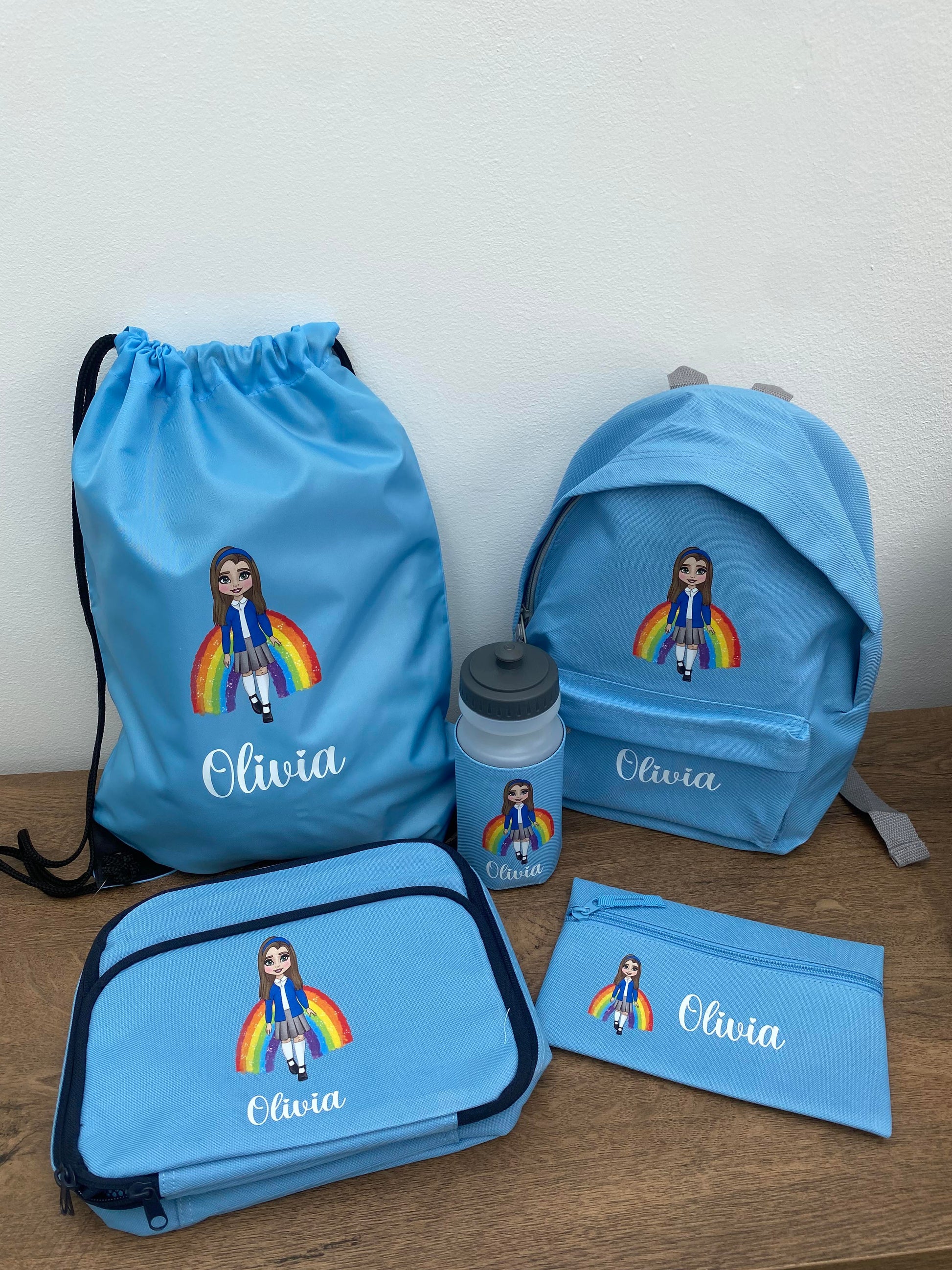 Customized school bundle set including a blue backpack, lunch bag, water bottle, drawstring PE bag, and pencil case, all featuring a personalized character design and the name 'Olivia'.