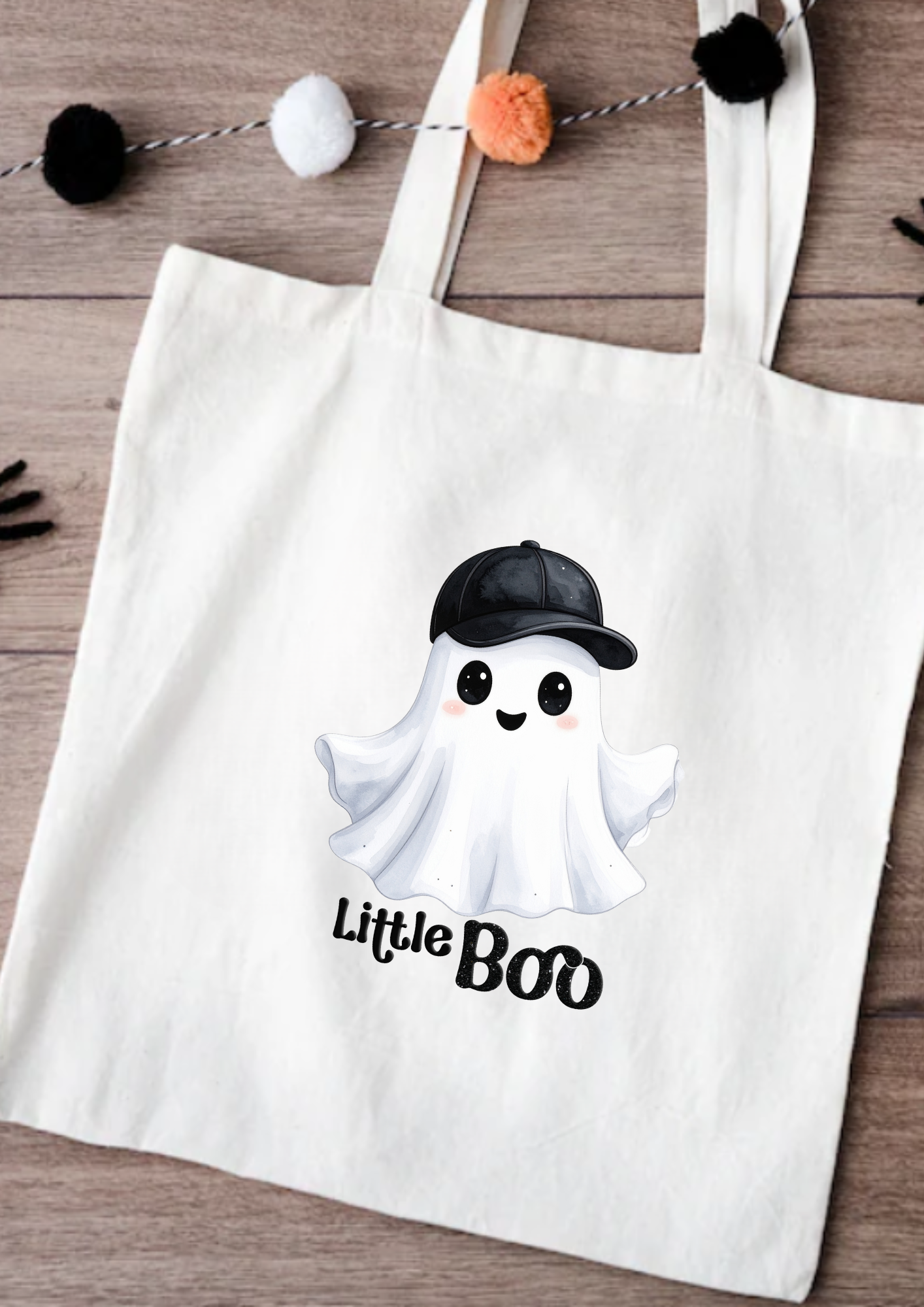 Tote bag with a ghost wearing a cap and 'Little Boo' text on a wooden surface.