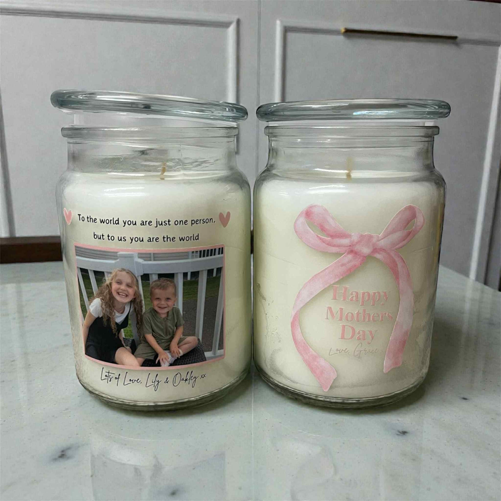 Two candles in glass jars with personalized messages and designs on a marble surface.