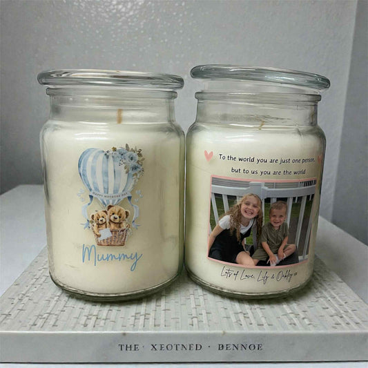 Two candles in glass jars with personalized designs and text on a textured surface.