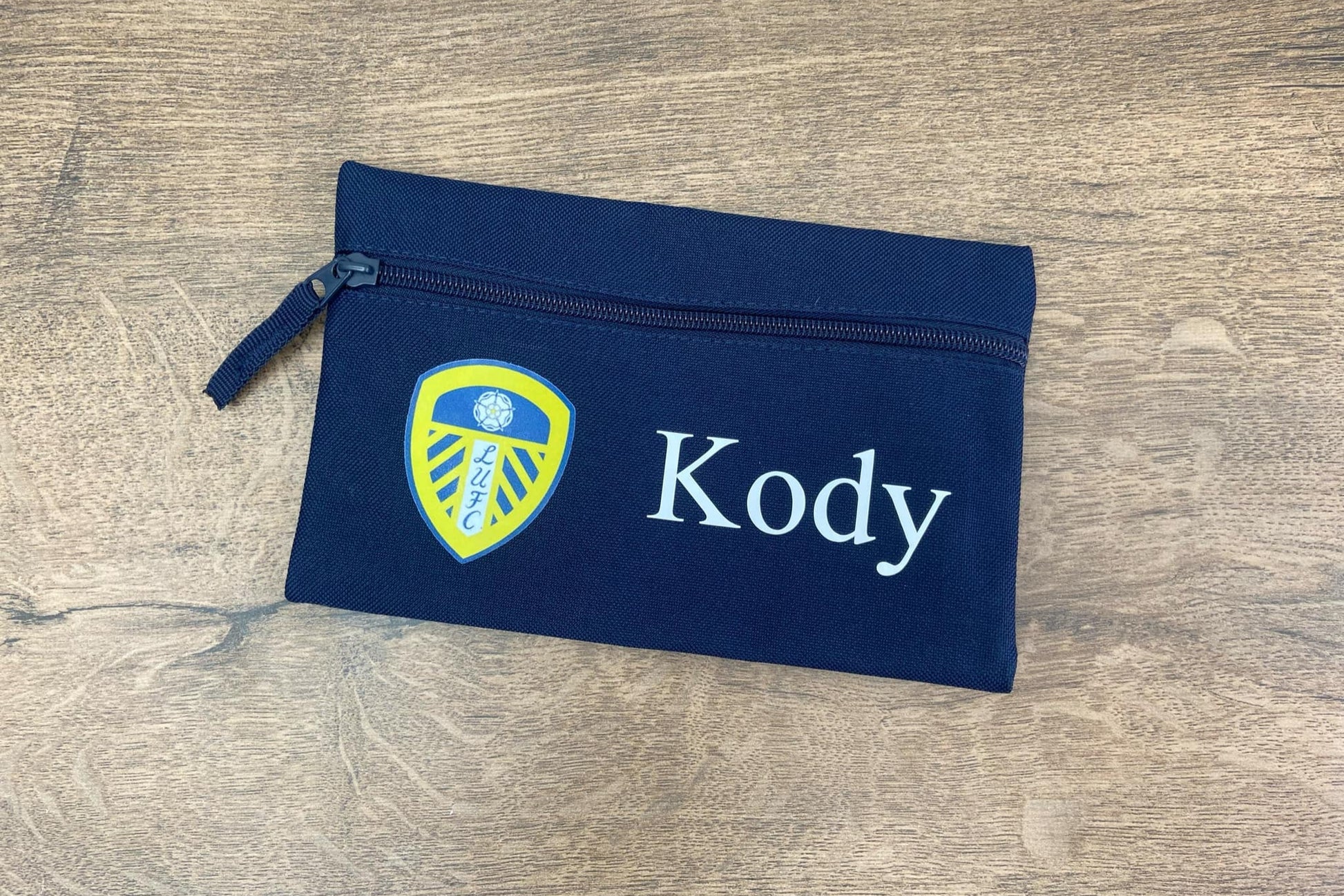 Navy blue pouch with a logo and 'Kody' text on a wooden surface