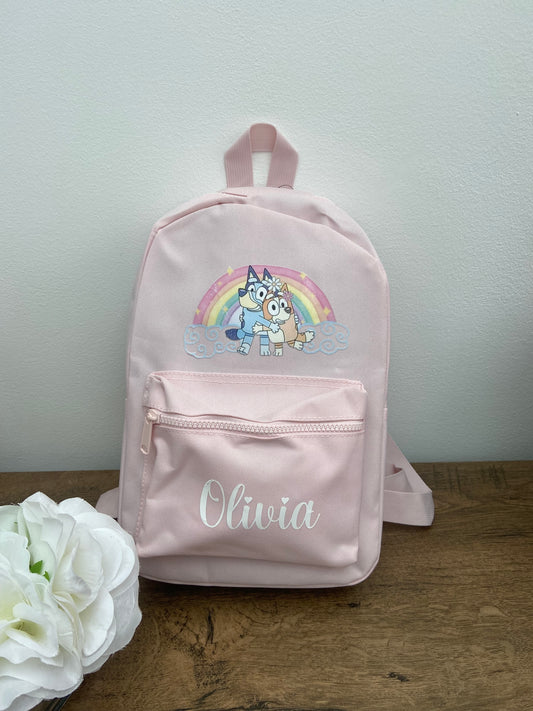 A pink personalised backpack for children with a rainbow and Bluey the dog design, featuring adjustable shoulder straps and the name 'Olivia' printed on the front.