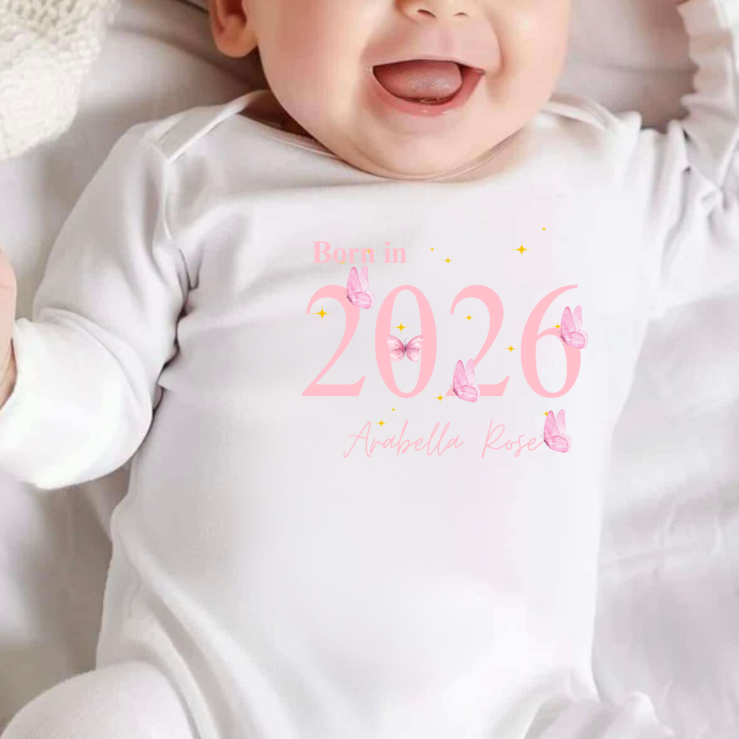 Baby wearing a white onesie with 'Born in 2026' text and butterfly graphics.