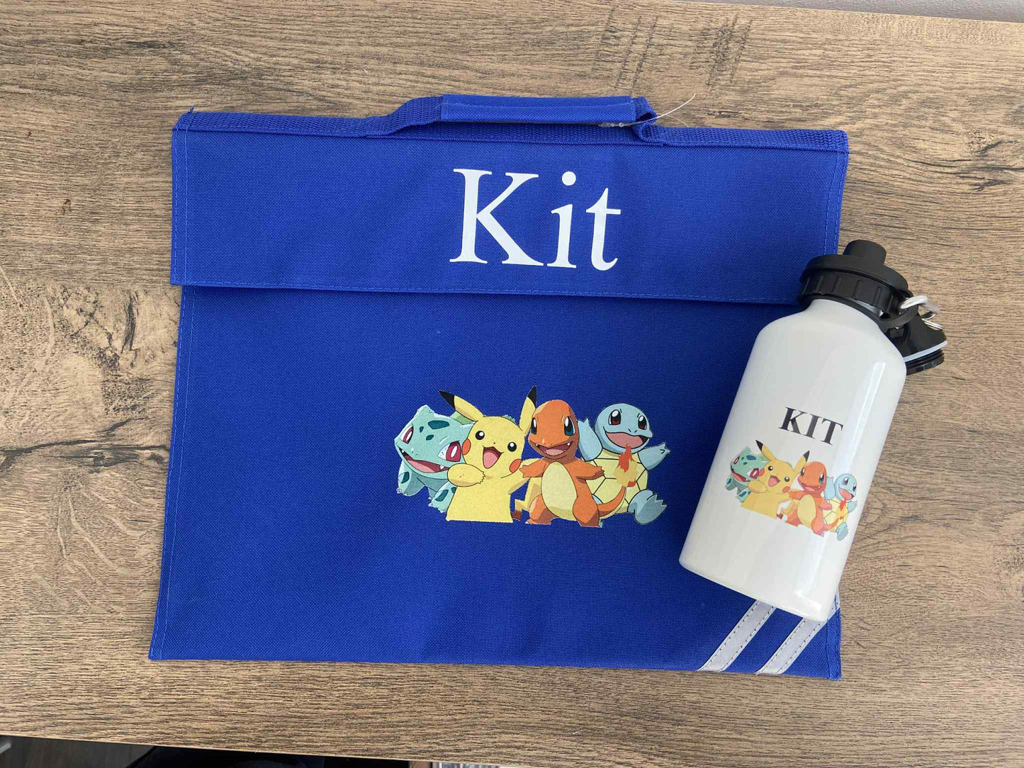 Blue Book bag with cartoon characters and 'Kit' text, next to a white water bottle with similar design on a wooden surface.