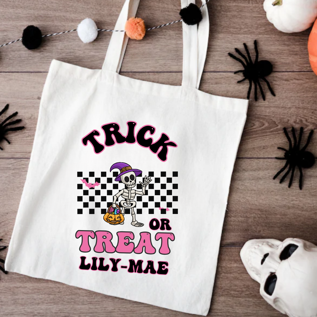 White tote bag with Halloween design and text on a wooden surface with decorative items.