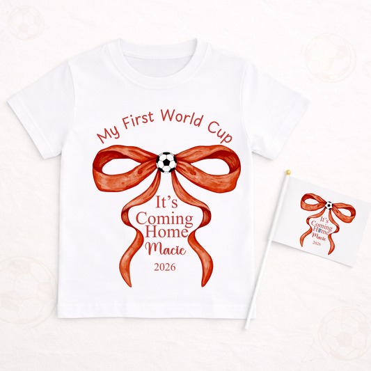 White t-shirt with red bow graphic and text 'My First World Cup It's Coming Home Macie 2026' on a white background