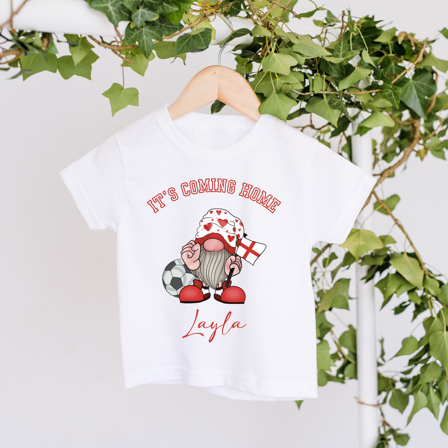White t-shirt with a gnome graphic and text on a hanger with greenery in the background