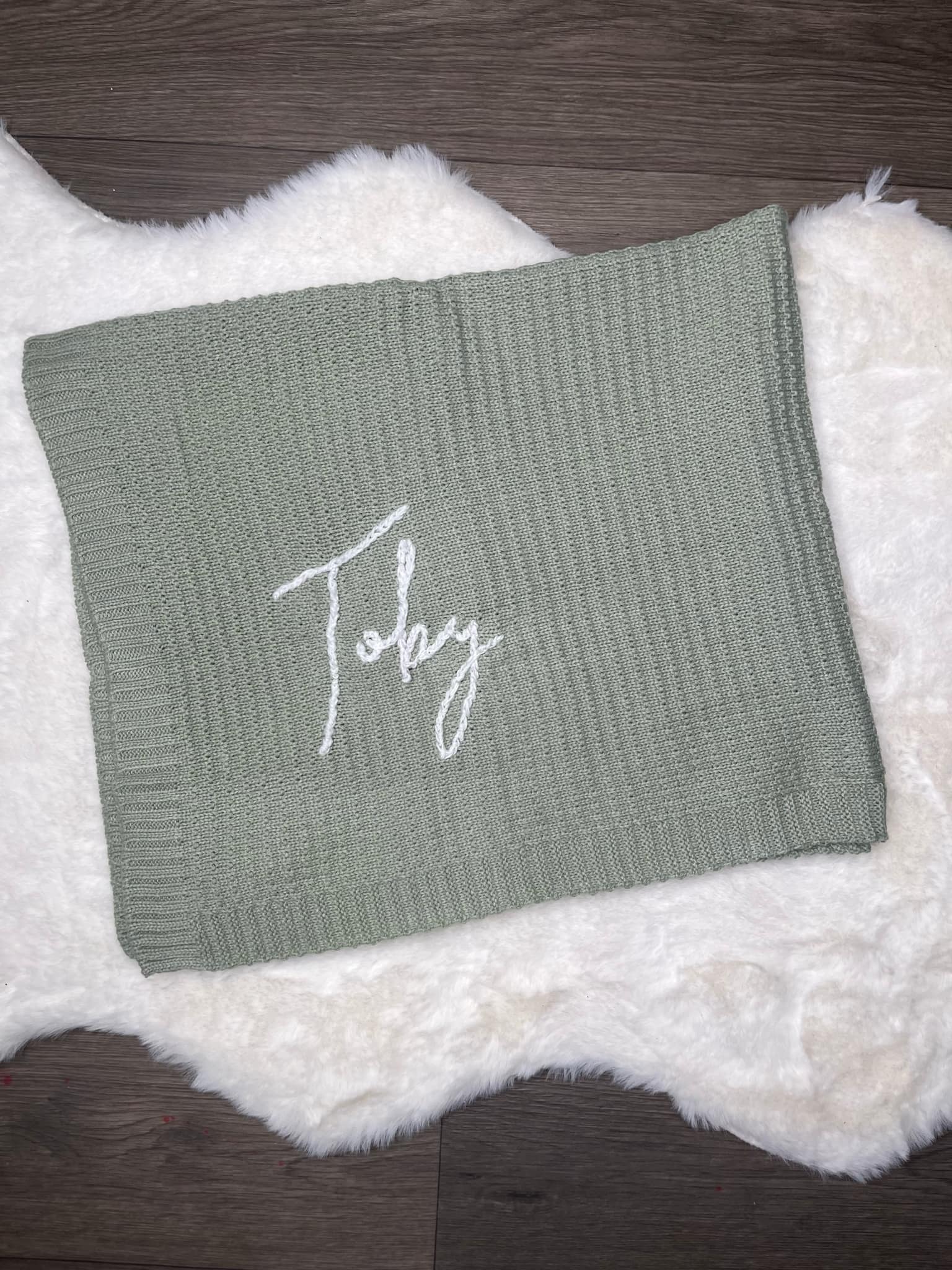 Green knitted blanket with 'Toby' embroidery on a textured surface