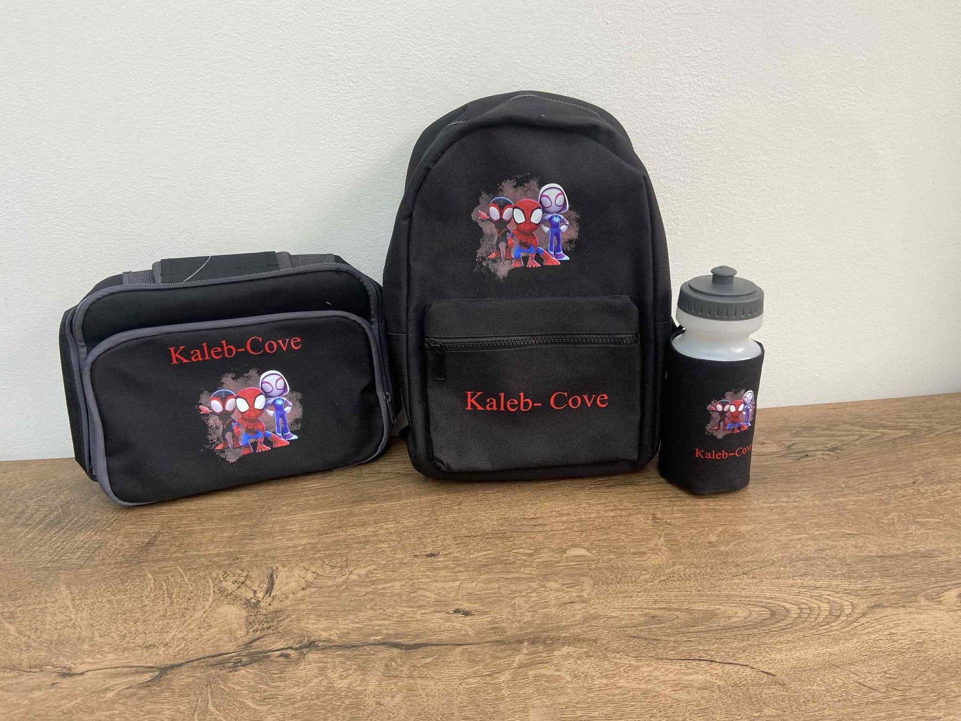 Black backpack, lunch bag, and water bottle with 'Kaleb Cove' branding on a wooden surface.