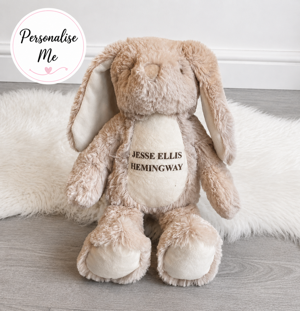 Personalised beige bunny teddy with custom printed name sitting on white rug and grey laminate flooring with personalise me badge.