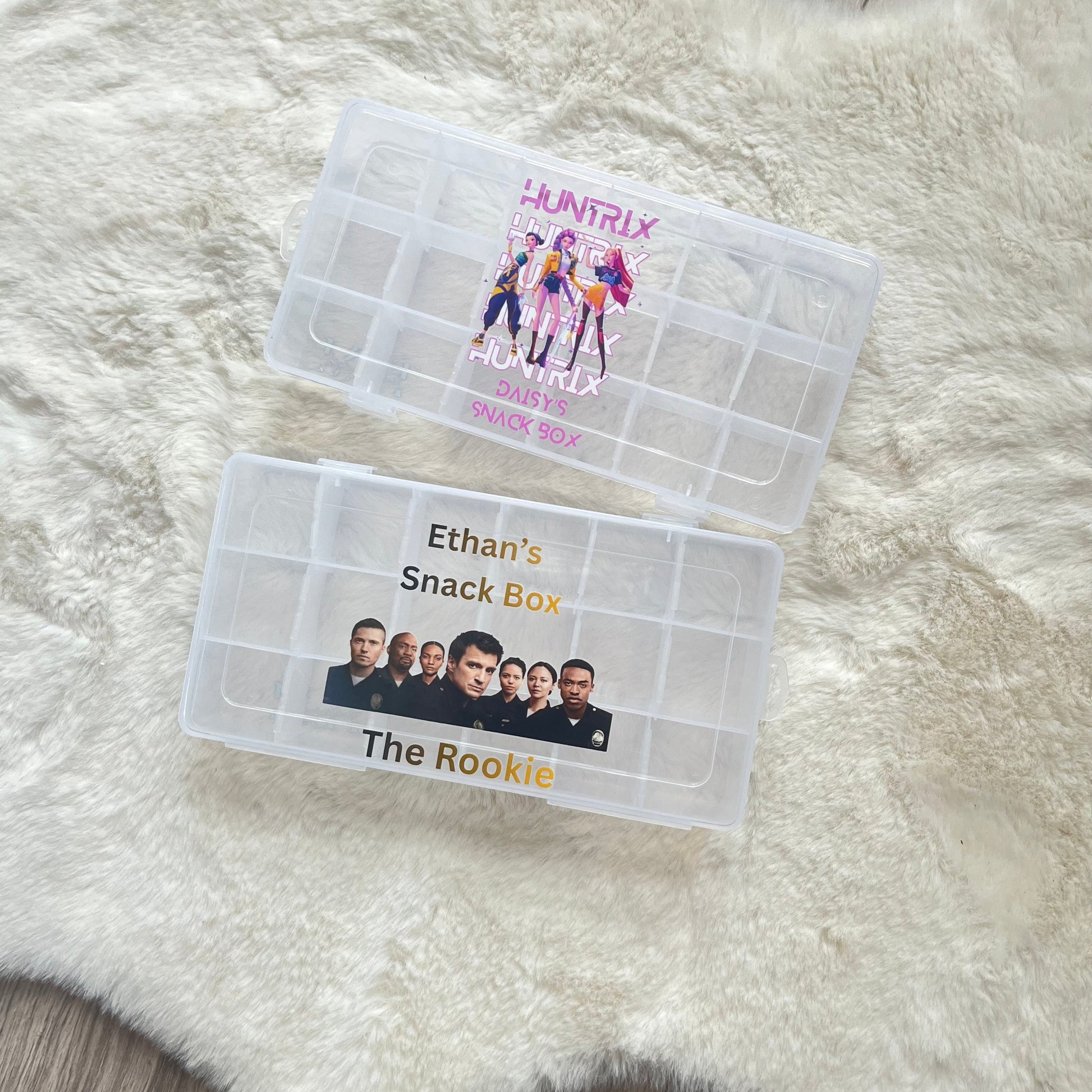 Two clear snack boxes with printed designs on a fluffy white surface.