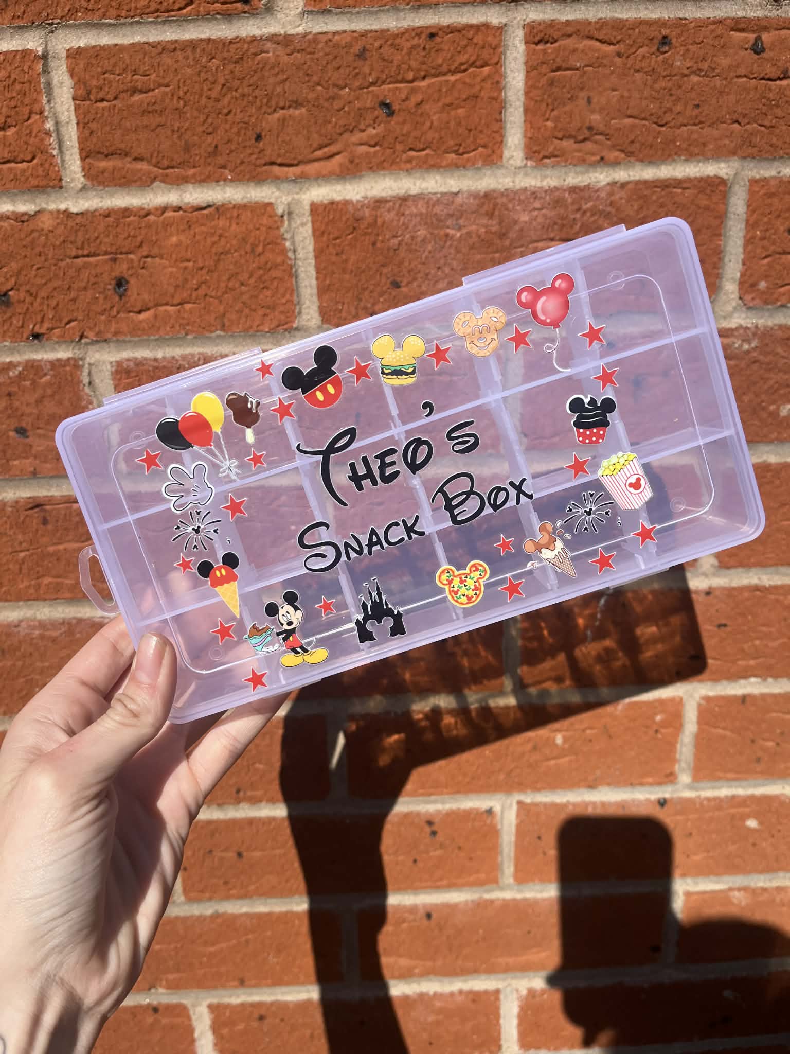 Transparent snack box with Mickey Mouse designs held against a brick wall