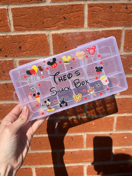 Transparent snack box with Mickey Mouse designs held against a brick wall
