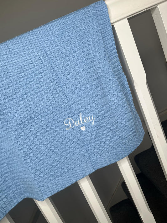 Blue baby blanket with 'Daley' embroidery on a crib