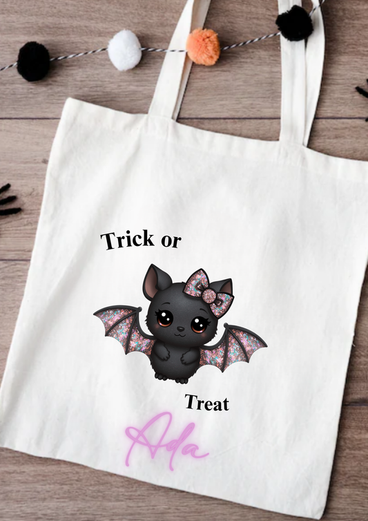 Tote bag with a bat design and 'Trick or Treat Ada' text on a wooden surface.