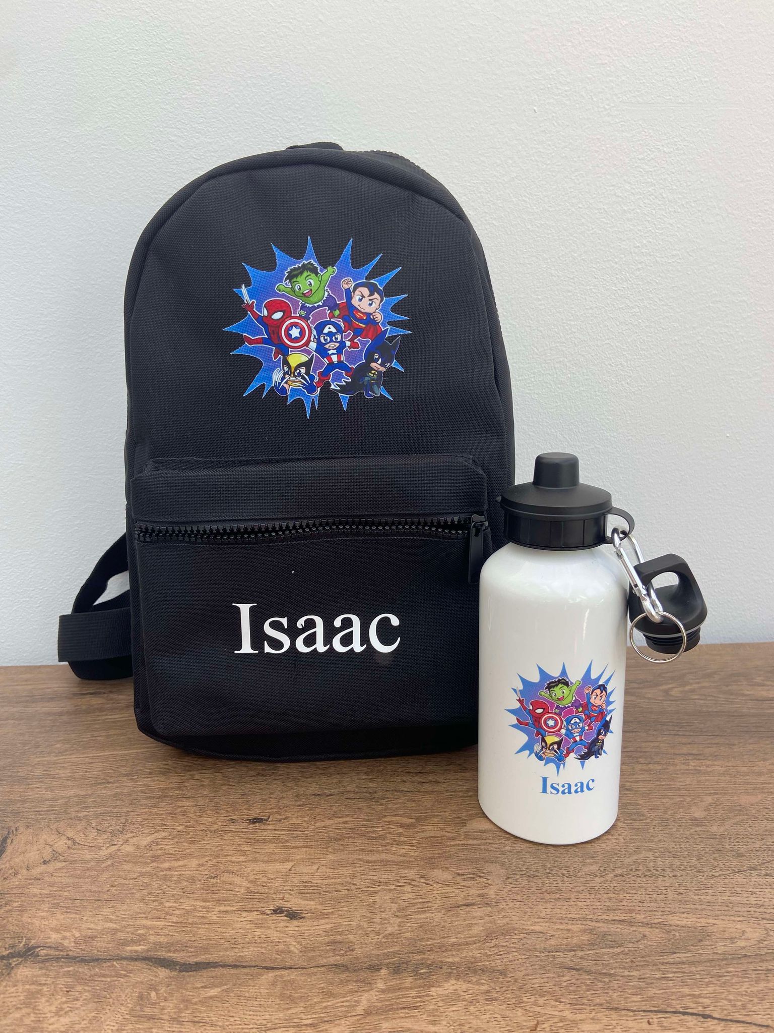 A black personalised mini backpack with a superhero design, a water bottle, and a name 'Issac' printed on the front.