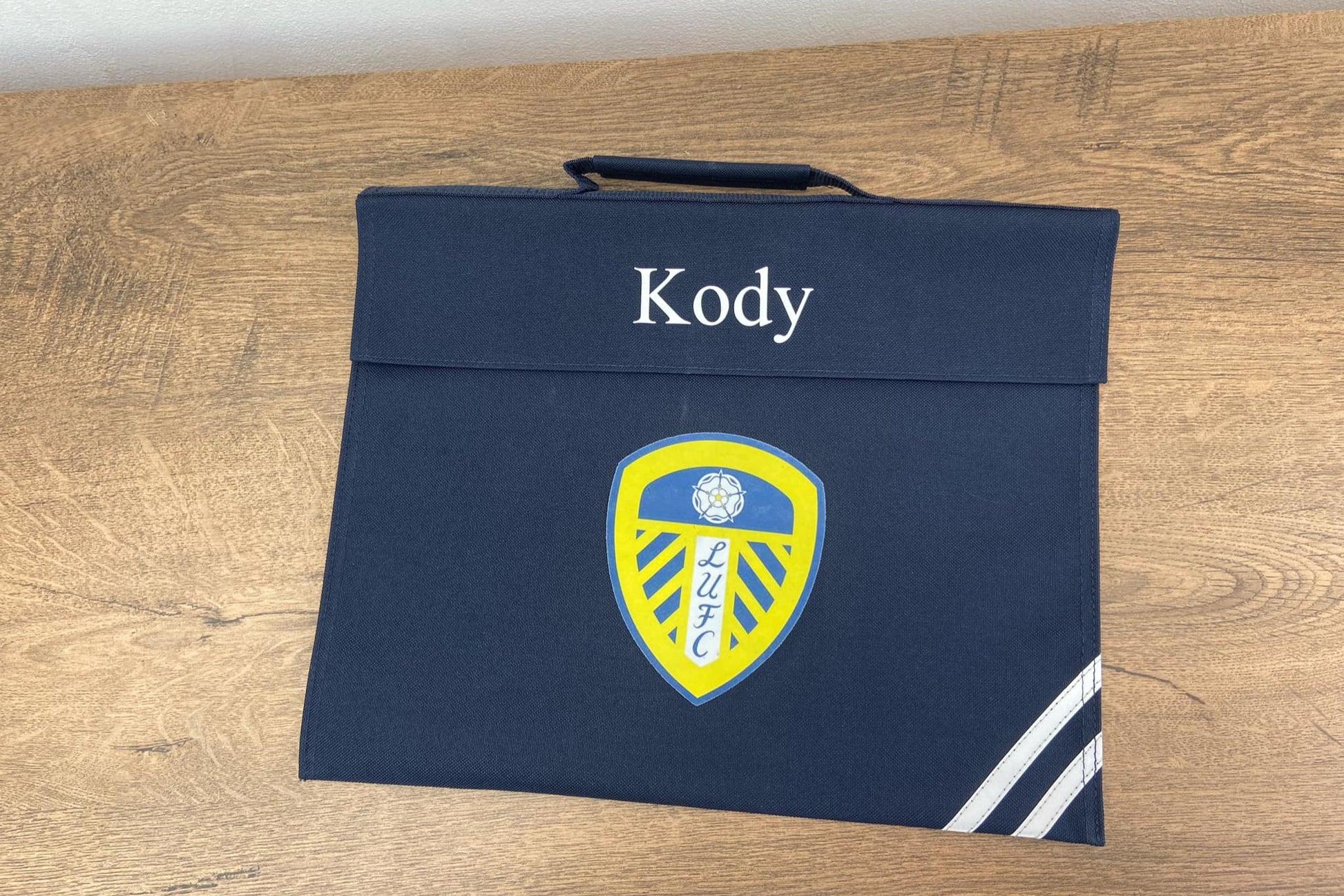 Navy blue bookbag with a logo and 'Kody' text on a wooden surface
