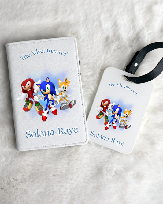 A personalized luggage tag set featuring Sonic the Hedgehog characters, displayed on a white faux fur background. The set includes a small white leatherette passport cover with a matching printed tag attached by a black strap.