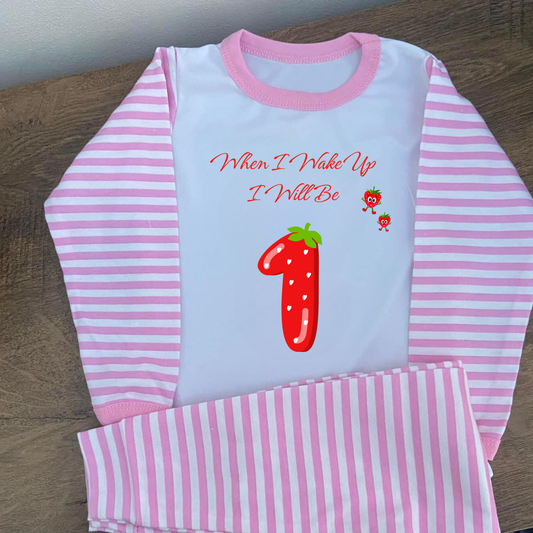 Children's pink and white striped pajama set with a red number one and text on a wooden surface.