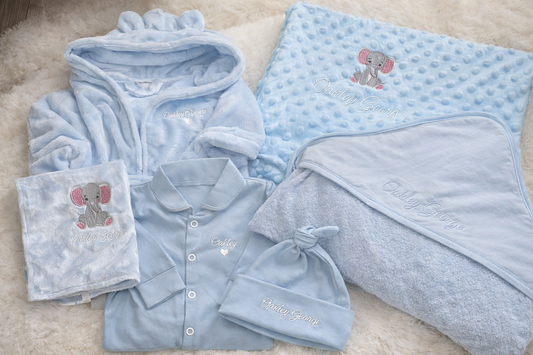 Baby clothing set with blue and gray items featuring elephant designs on a soft surface.