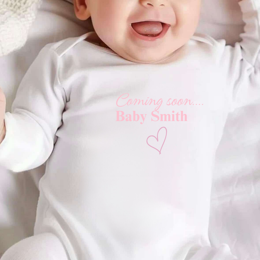 Personalised White Baby sleepsuit with pink text saying coming soon baby smith