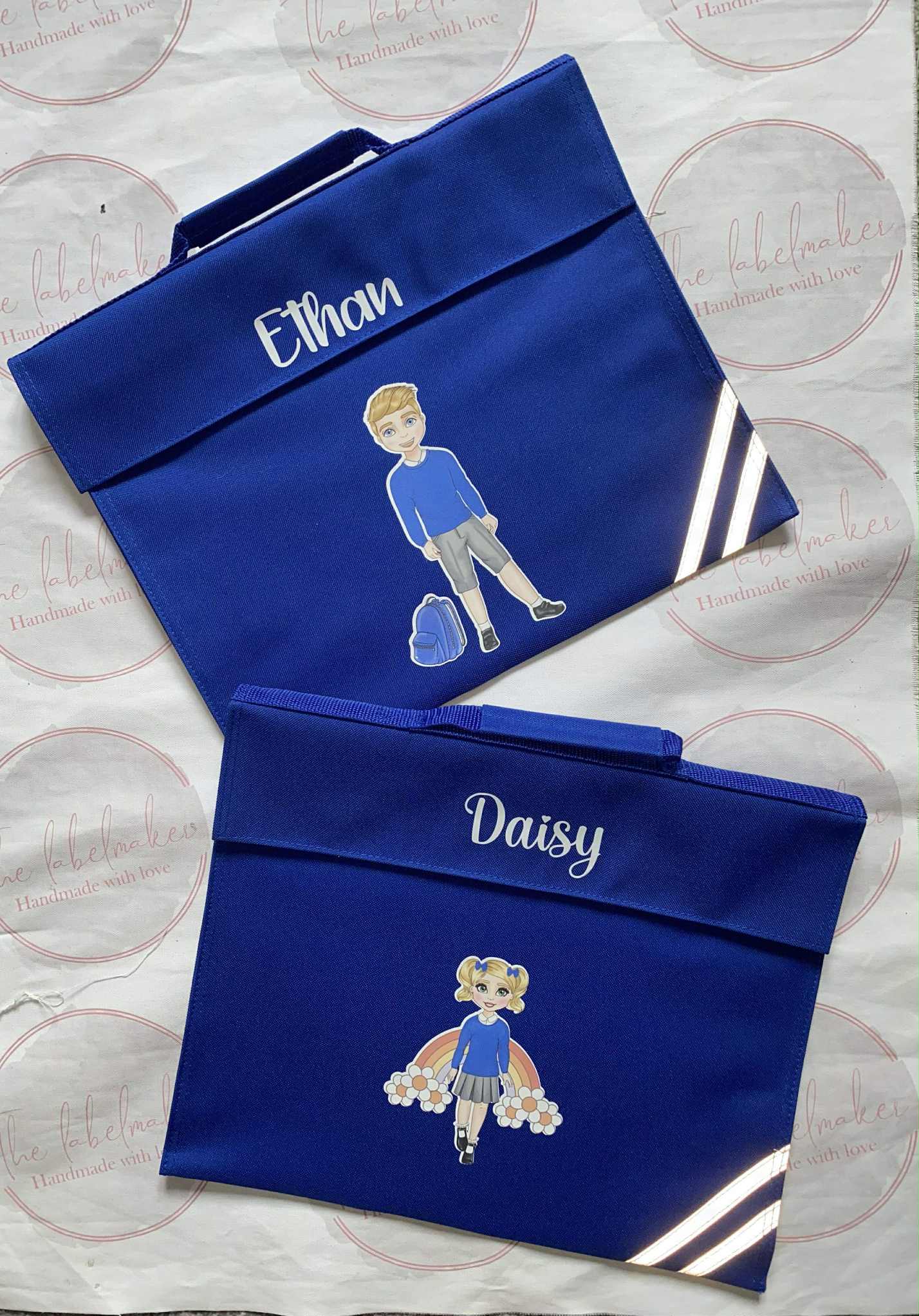 Two blue bags with embroidered names and illustrations on a patterned background