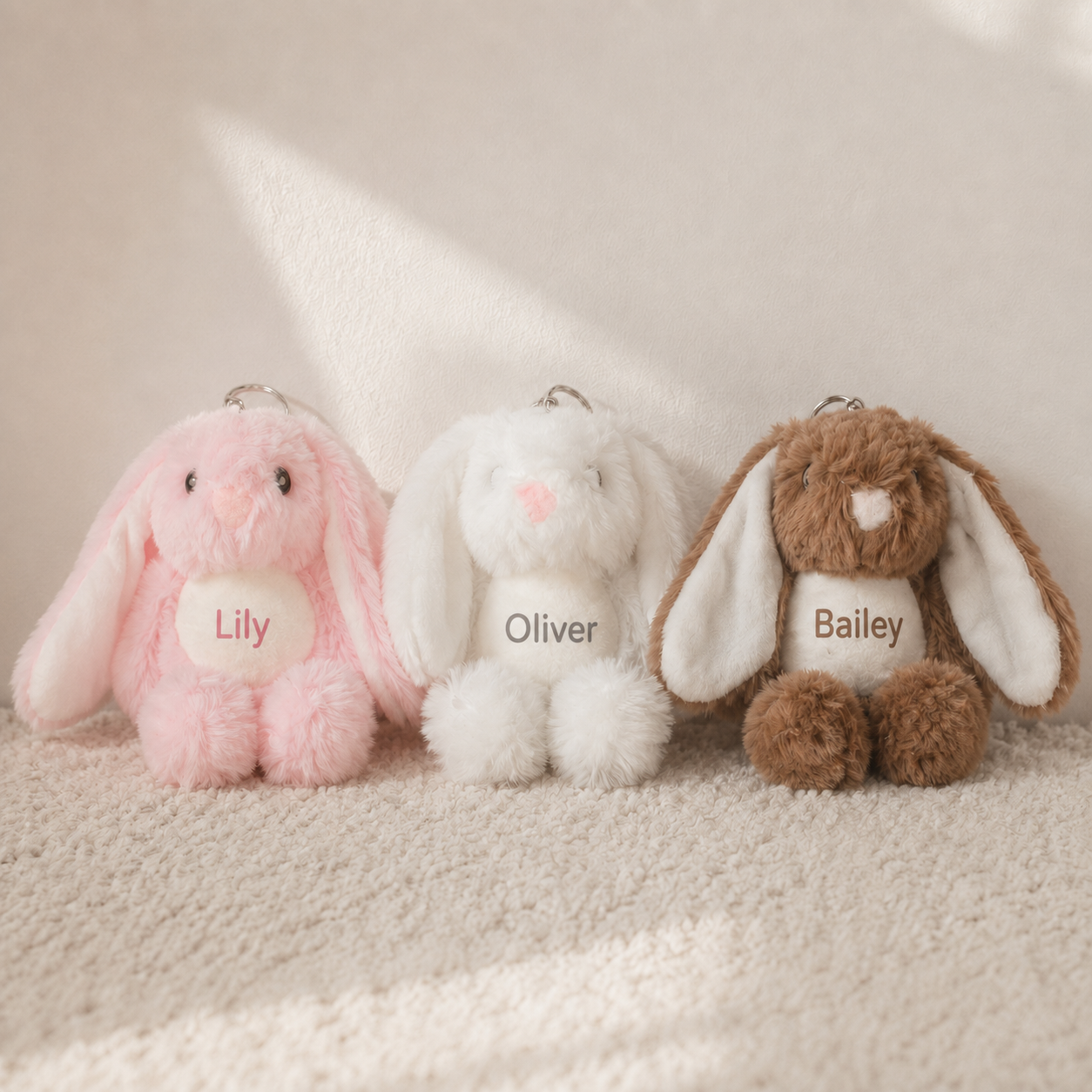 Three personalised plush bunny keyrings in pink, white and brown, printed with the names Lily, Oliver and Bailey.
