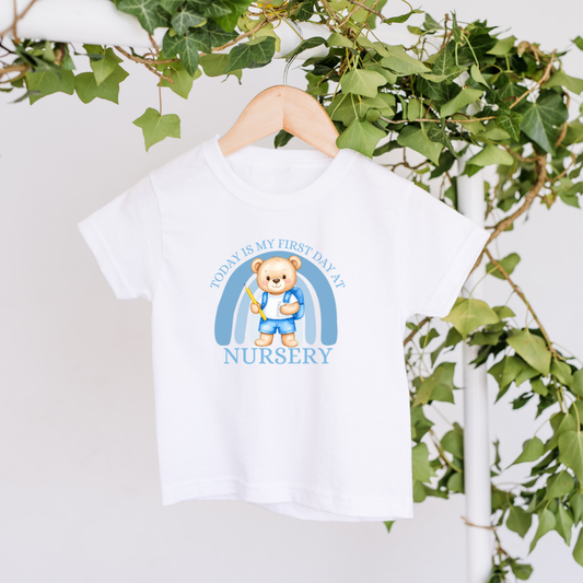 White t-shirt with a teddy bear design and text on a hanger with green leaves in the background