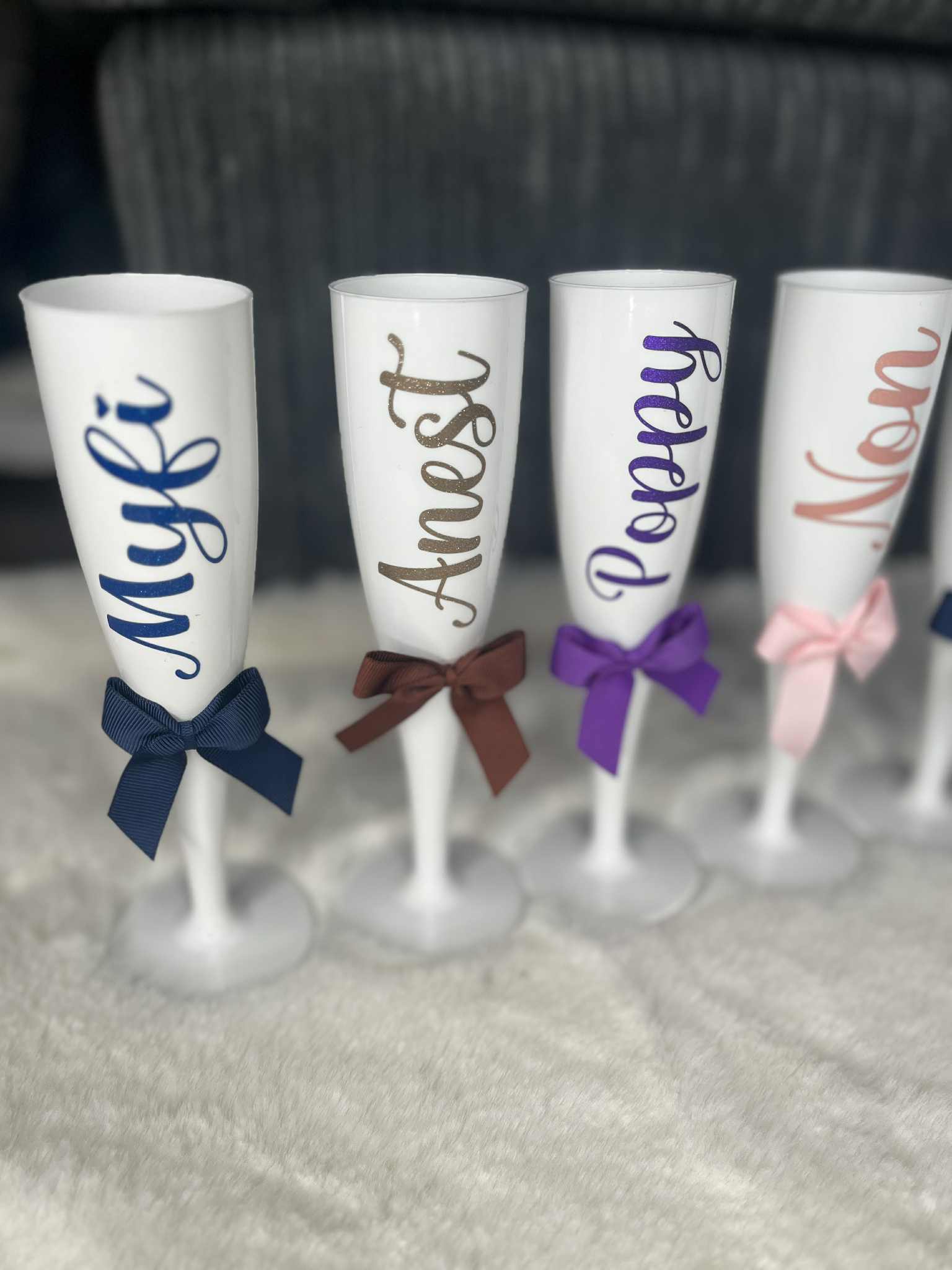 Four white champagne flutes with personalised names and colourful bows for a prom day.