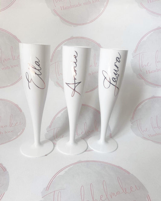 A set of white champagne flutes, each with a different name written in a script font on the side.