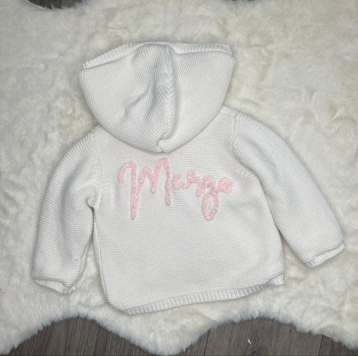 White baby hoodie with pink text on a fluffy white surface