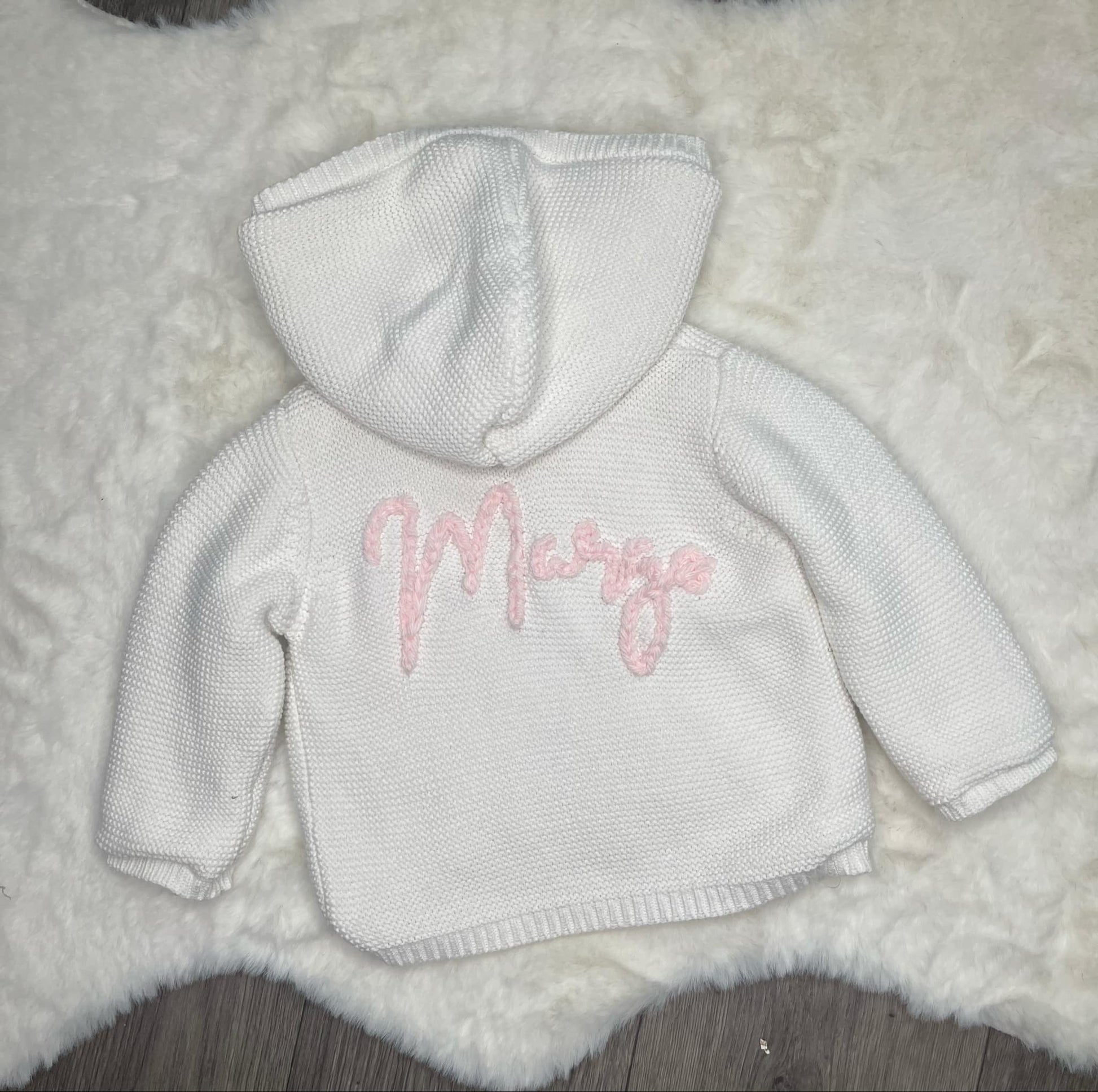 White baby hoodie with pink text on a fluffy white surface