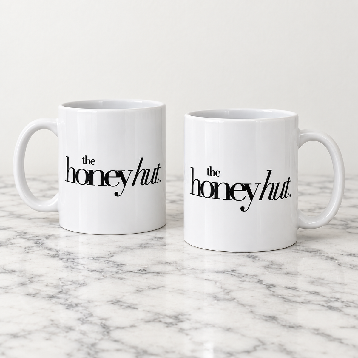 Two white ceramic business mugs printed with The Honey Hut black logo