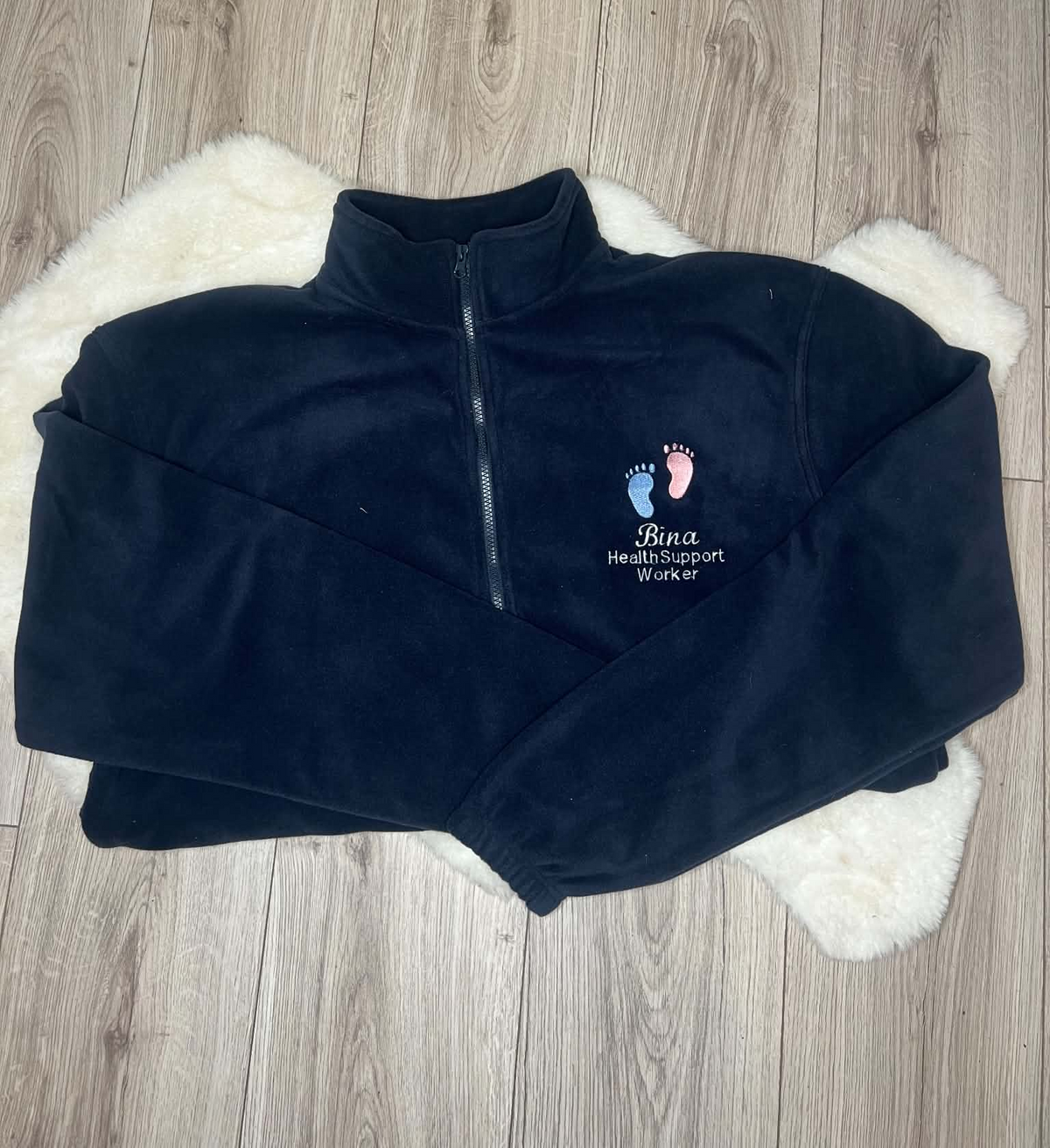 Navy fleece with pink and blue baby footprints embroidered above Bina and Health Support Worker wording