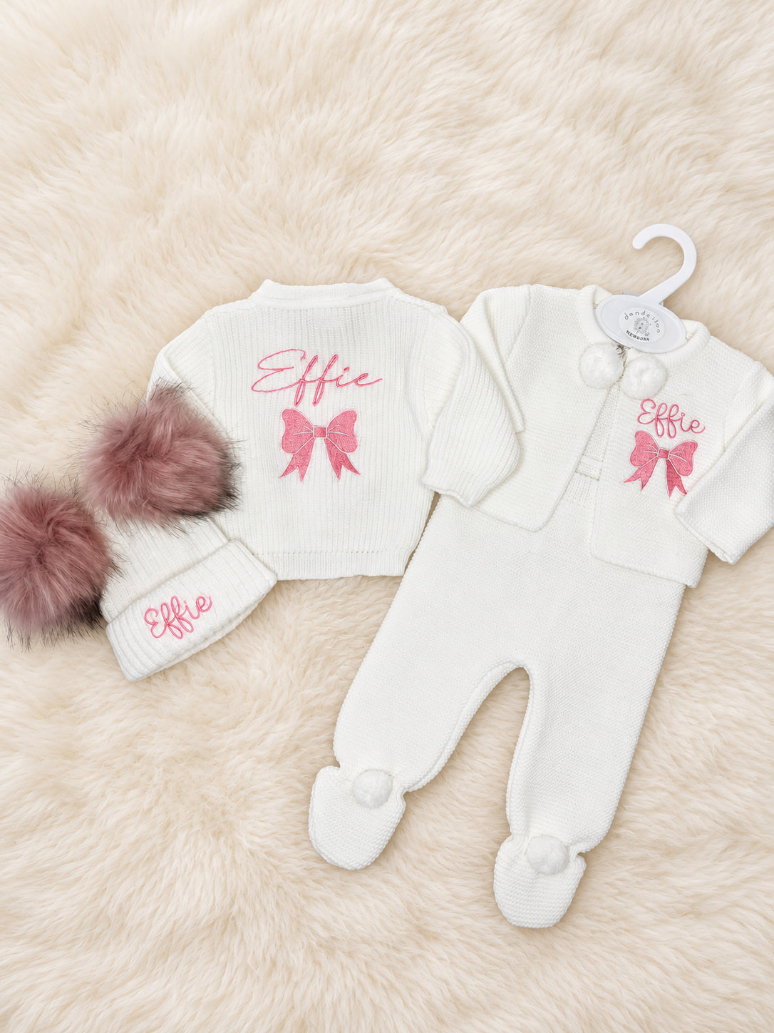 White knitted baby cardigan, pom pom outfit and double pom pom hat embroidered with Effie in pink.