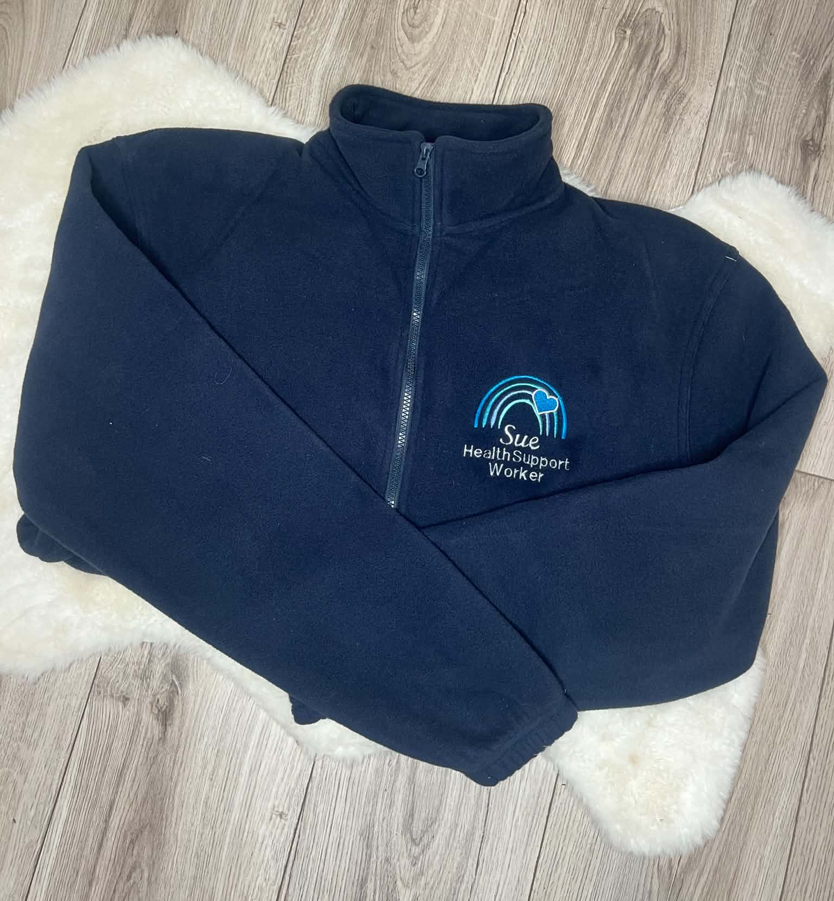 Navy fleece with blue rainbow and heart embroidery above Sue and Health Support Worker wording