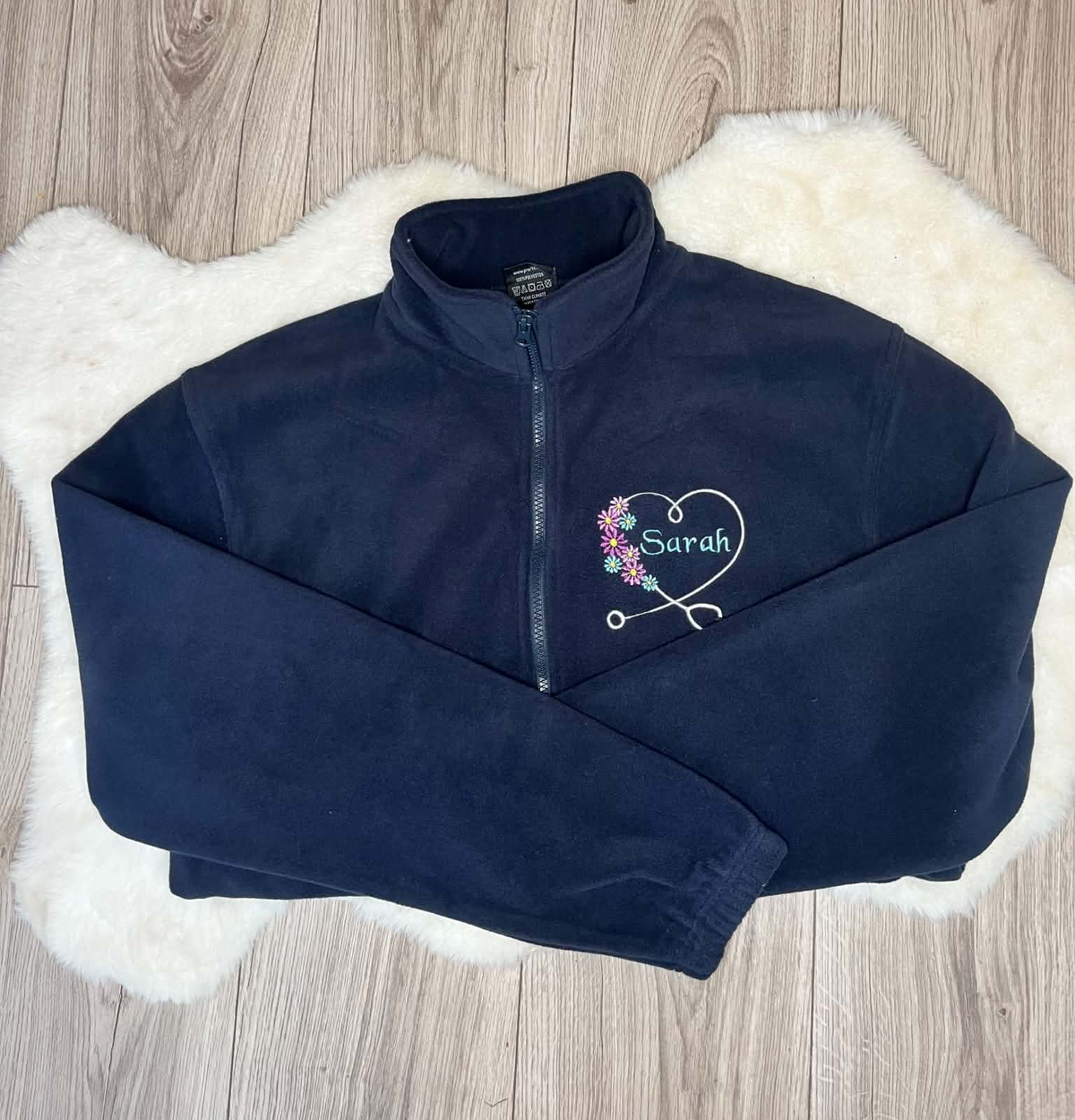 Navy fleece embroidered with a white stethoscope heart, colourful flowers and Sarah name