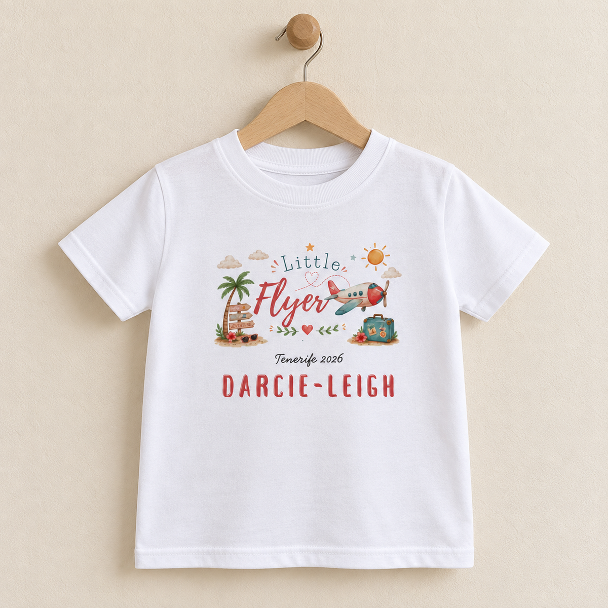 Personalised Little Flyer children's white T-shirt displayed on a wooden hanger against a warm beige background