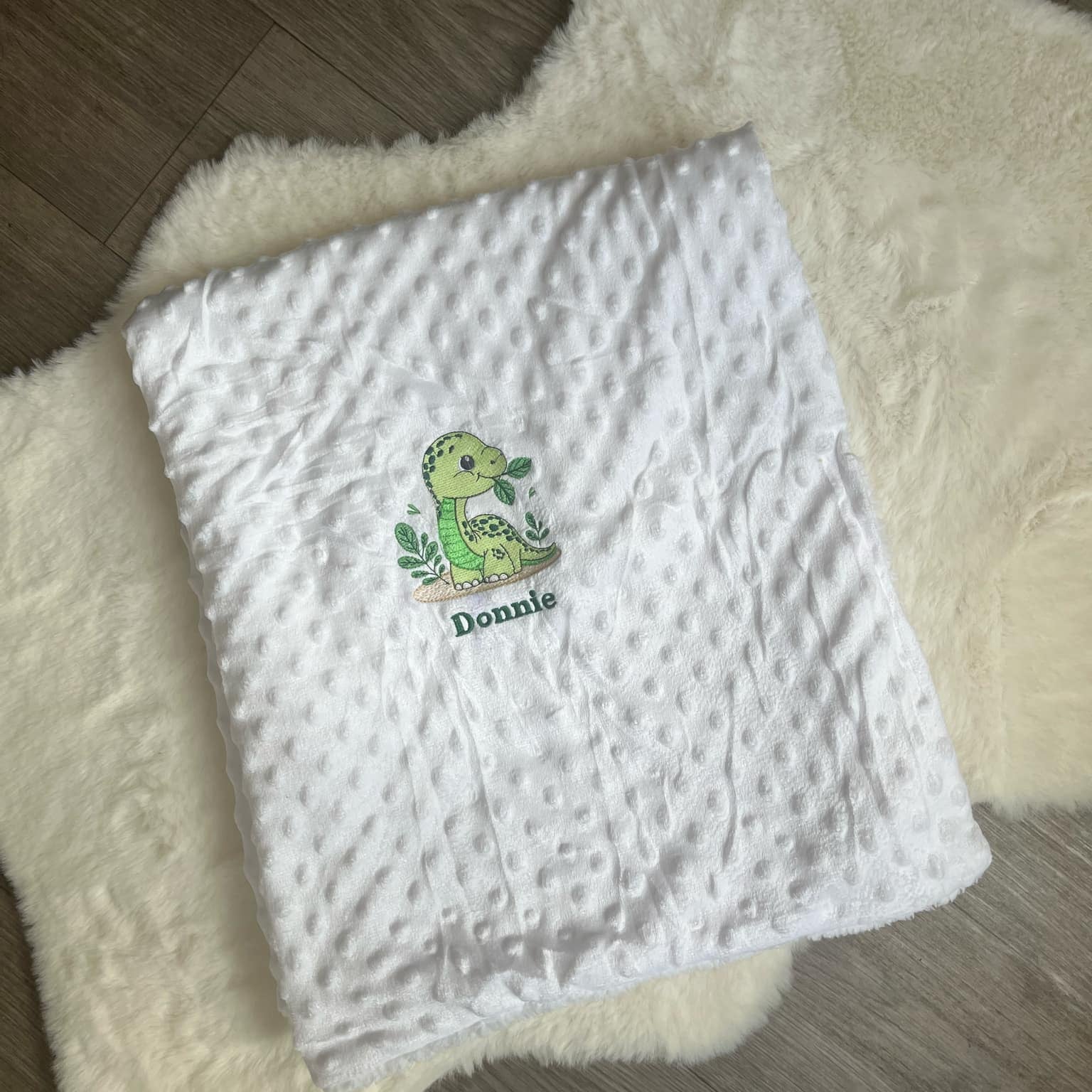 White textured blanket with a green dinosaur design and 'Donnie' text on a fluffy white surface.